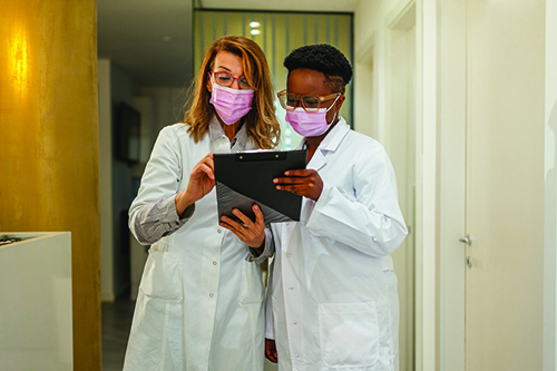 Two female laboratorians in masks holding and looking at a clipboard.