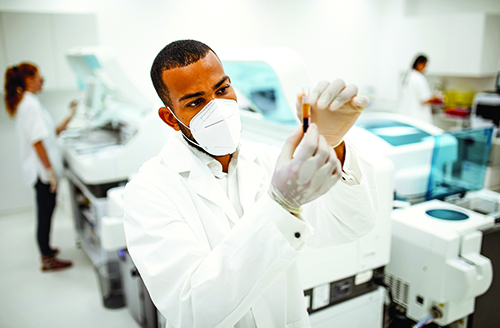 A male, African American laboratorian holding and examining a blood sample.