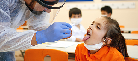 Pediatrician taking saliva test from children with face masks in a school