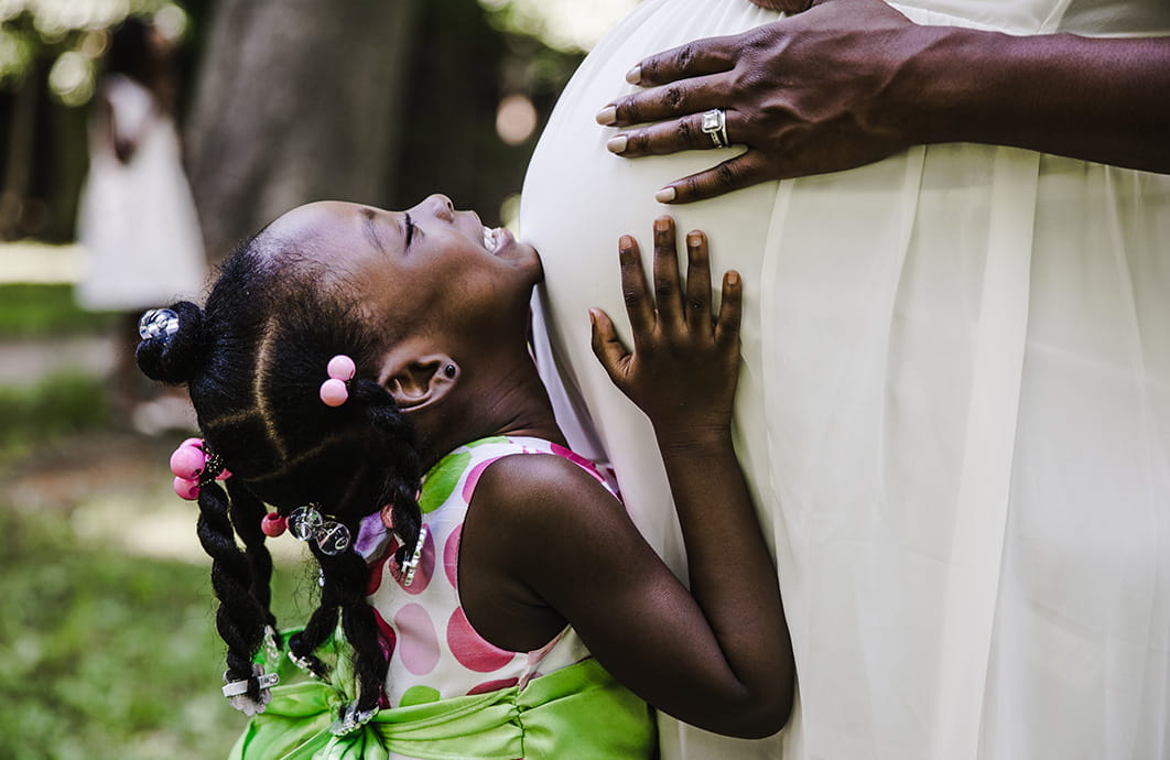 Child pressed against her mother's pregnant belly and looking up smiling