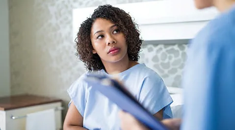 A patient in a gown looks up at a medical professional holding a folder