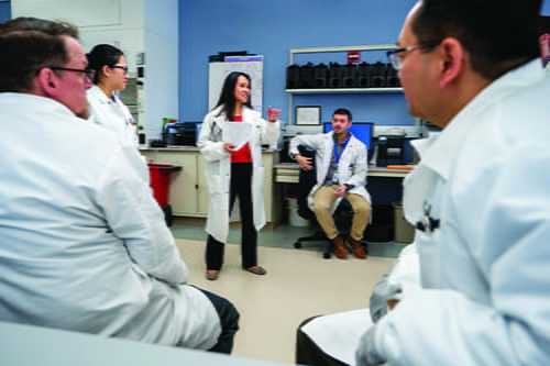 A female laboratorians speaking to other laboratorians around her