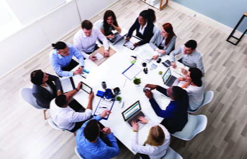 A birdseye view of a group of people sitting at a table with computers and tablets.