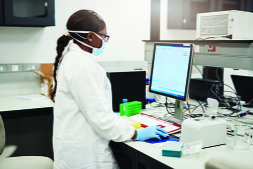 A female, African American laboratorian standing at a computer.