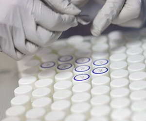 two hands in white gloves labeling testing tubes